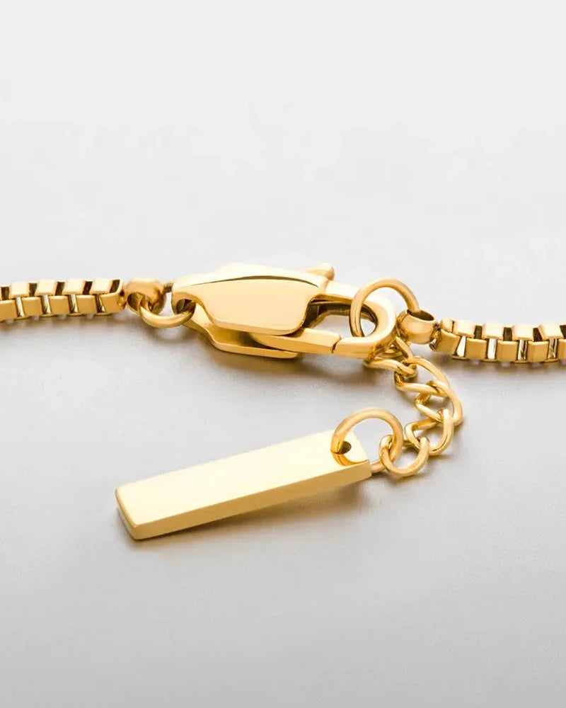 Gold bracelet with a tag charm on a light gray background