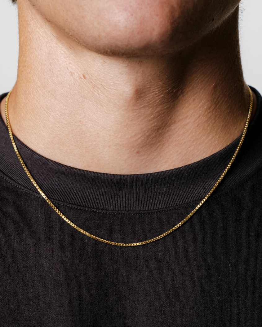 Gold chain necklace worn by a person on a black background