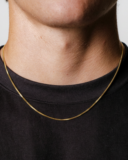 Gold chain necklace worn by a person on a black background